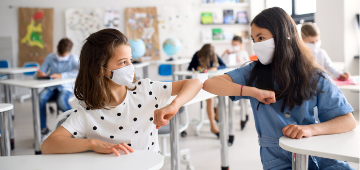 Two students in class wearing masks greeting each other by touching elbows